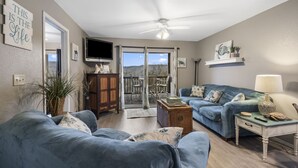 A living room with two blue sofas, a wooden cabinet, a television, and a ceiling fan. - Walk-In 2BR Lakeview Condo | Near SDC (Branson)