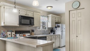 A kitchen with white cabinetry, a central island, a microwave, a stove, a sink, and a refrigerator.