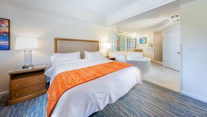 Habitació d'hotel amb un llit gran, una tauleta de nit, una làmpada, un bany amb banyera i dutxa.