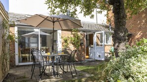 A patio with a table and chairs, a large umbrella, and a brick wall.