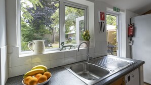 A kitchen with a double sink, a window with a view of greenery, and a bowl of fruit on the counter.