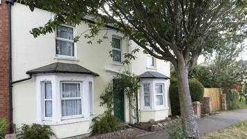 A two-story house with a green door, white windows, and a tree in front.