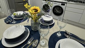 Una cucina moderna con elettrodomestici in acciaio inossidabile, zoccolo di marmo e zona pranzo apparecchiata con piatti bianchi e blu scuro, posate e un vaso con fiori.