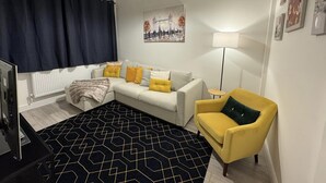 Un soggiorno moderno con divano, poltrona gialla, tappeto nero fantasia e un quadro raffigurante un paesaggio urbano.