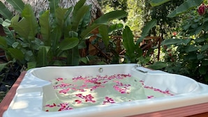 A hot tub filled with water and rose petals, surrounded by lush greenery. - Samana Tropical with DodoMap (Samaná)