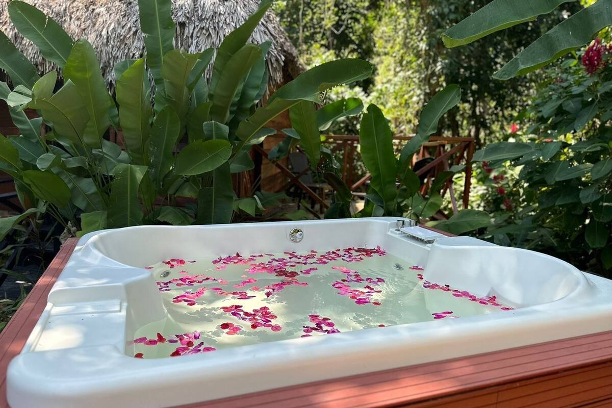 A hot tub filled with water and rose petals, surrounded by lush greenery.