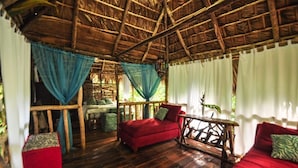 A rustic wooden room with a thatched roof, red sofas, and a small table. - Samana Tropical with DodoMap (Samaná)