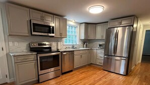 A modern kitchen with stainless steel appliances, wooden flooring, and white cabinetry. - Cape Cod Fun - Entire home 3BR up to 9 guests  (Barnstable)