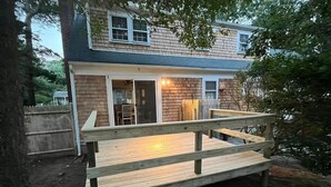 A wooden deck with a railing in front of a house with a sliding glass door and a small porch. - Cape Cod Fun - Entire home 3BR up to 9 guests  (Barnstable)