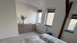 A spacious bedroom with a large bed, a wooden dresser, and a small window. - Ferienwohnung in Obernkirchen (Obernkirchen)