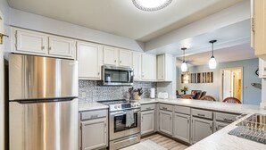 A modern kitchen with stainless steel appliances, a tiled backsplash, and light-colored cabinetry. - Lakefront Condo w/ Resort Amenities in Osage Beach (Osage Beach)
