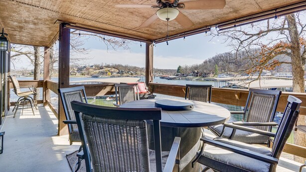A covered outdoor seating area with a table and chairs, overlooking a body of water and a distant landscape. - Lakefront Condo w/ Resort Amenities in Osage Beach (Osage Beach)