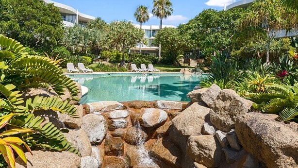 A pool area with lounge chairs, a waterfall feature, and lush greenery.