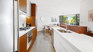 A modern kitchen with wooden cabinets, a white countertop, and a dining area with a table and chairs.