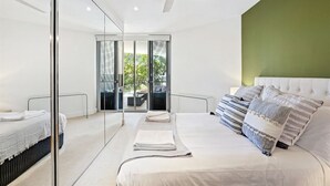 A modern bedroom with a large bed, a ceiling fan, and a view through glass doors to an outdoor area.