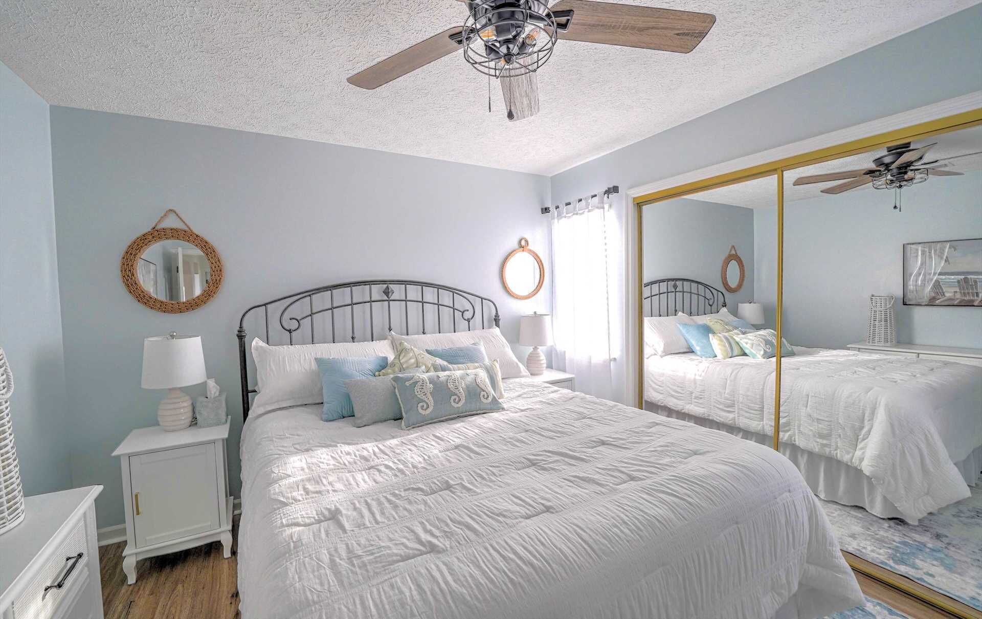 Une chambre à coucher avec un grand lit, une table de chevet, un miroir et un ventilateur de plafond.
