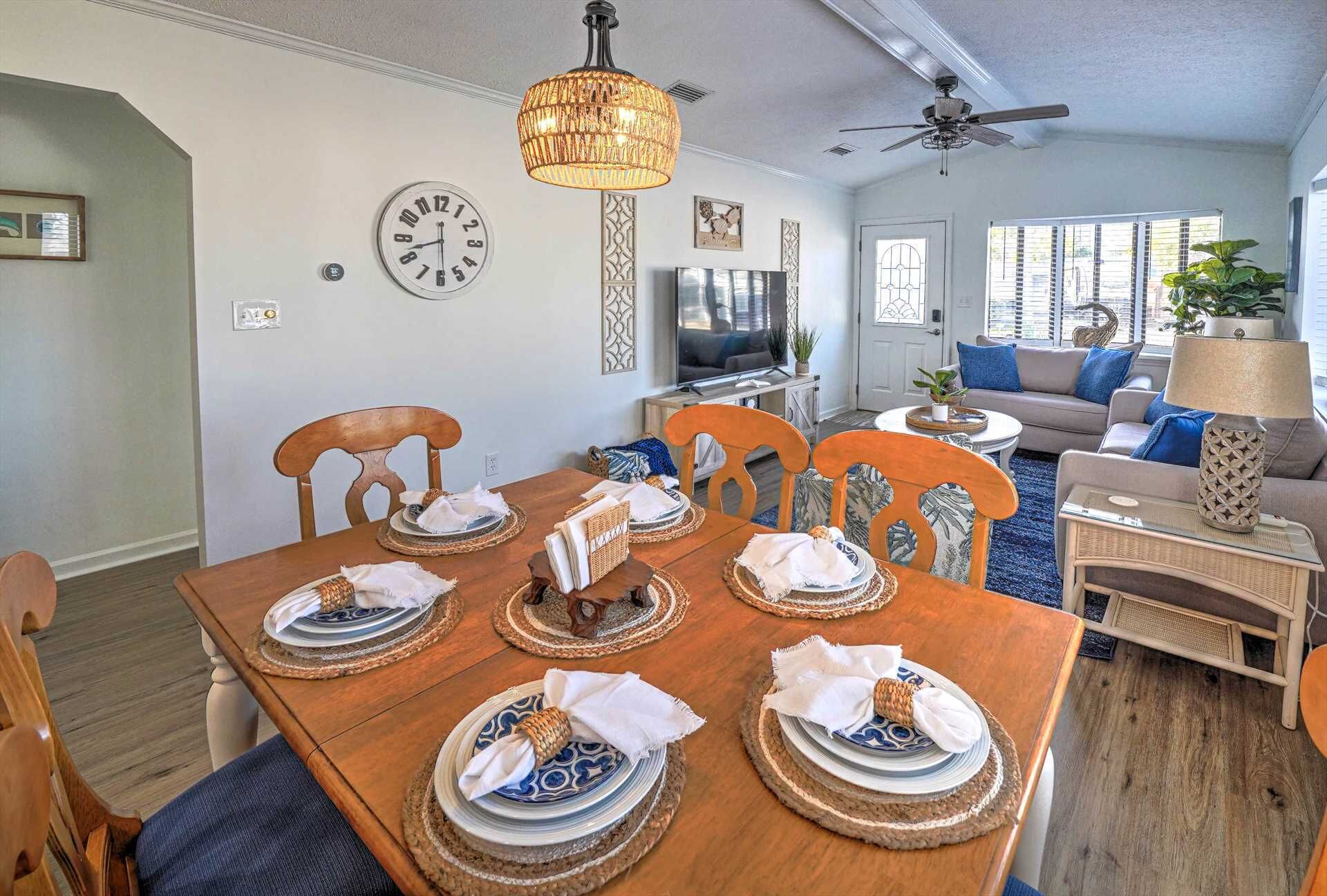 A dining area with a wooden table set for six, a television in the background, and a living area with a sofa and a lamp.
