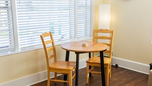 A room with a round wooden table and two wooden chairs, a window with blinds, and a wall-mounted light fixture. - NEW Listing! In the Heart of Jax Beach (Jacksonville Beach)