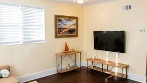 A living room with a flat-screen TV mounted on the wall, a wooden coffee table, a sofa, and a painting of a beach scene. - NEW Listing! In the Heart of Jax Beach (Jacksonville Beach)