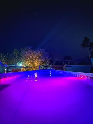 Área de piscina en la azotea con fuente de agua y un árbol iluminado.