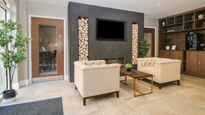 Uma sala de estar moderna com lareira, dois sofás, uma mesa de centro e uma TV instalada em uma parede de mármore.