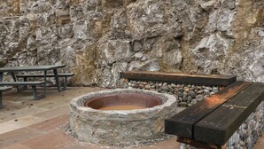 Um fogo de pedra com um banco e mesas de piquenique num pátio.