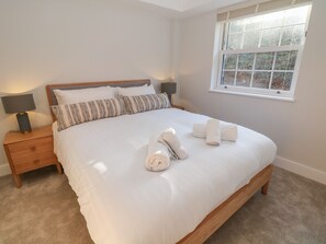 A neatly made bed with white linens and rolled towels, a wooden headboard, and a nightstand with a lamp. - Rock Mill Apartment (Hope Valley)