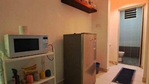 Een kleine keuken met een magnetron, koelkast en een plank met diverse spullen.