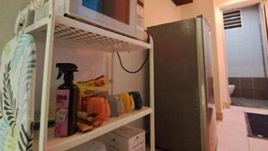 Een kleine keuken met een magnetron, een koelkast en een plank met schoonmaakspullen.