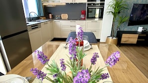 A modern kitchen with white cabinets, a built-in oven, and a dining area with a wooden table set for two. - Luxury house Prestige (Split)