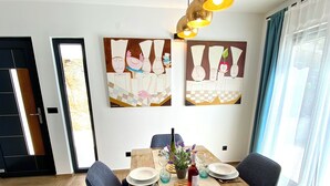A dining area with a wooden table set for four, surrounded by chairs, with artwork on the walls and a view of the outdoors through a window. - Luxury house Prestige (Split)
