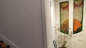 Eine Treppe mit Holzwertlauf, ein Stuhl und ein Blumentopf in der Nähe einer Tür mit Buntglasfenstern.