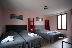 Two single beds with grey bedding and white towels, a small table, and a shelving unit in a stylish room.