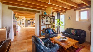 A spacious living area with a wooden ceiling, leather sofas, a wooden coffee table, and a bookshelf with decorative items. - Ty Jane Dour - Maison avec jardin (Plouhinec)