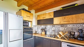 A compact kitchen with a refrigerator, oven, microwave, and dishwasher. It features wooden cabinets, a tiled backsplash, and a wooden countertop. - Ty Jane Dour - Maison avec jardin (Plouhinec)