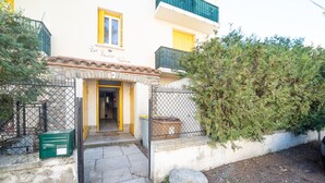 A two-story building with a yellow door and a small porch. There is a green mailbox and a trash bin outside.