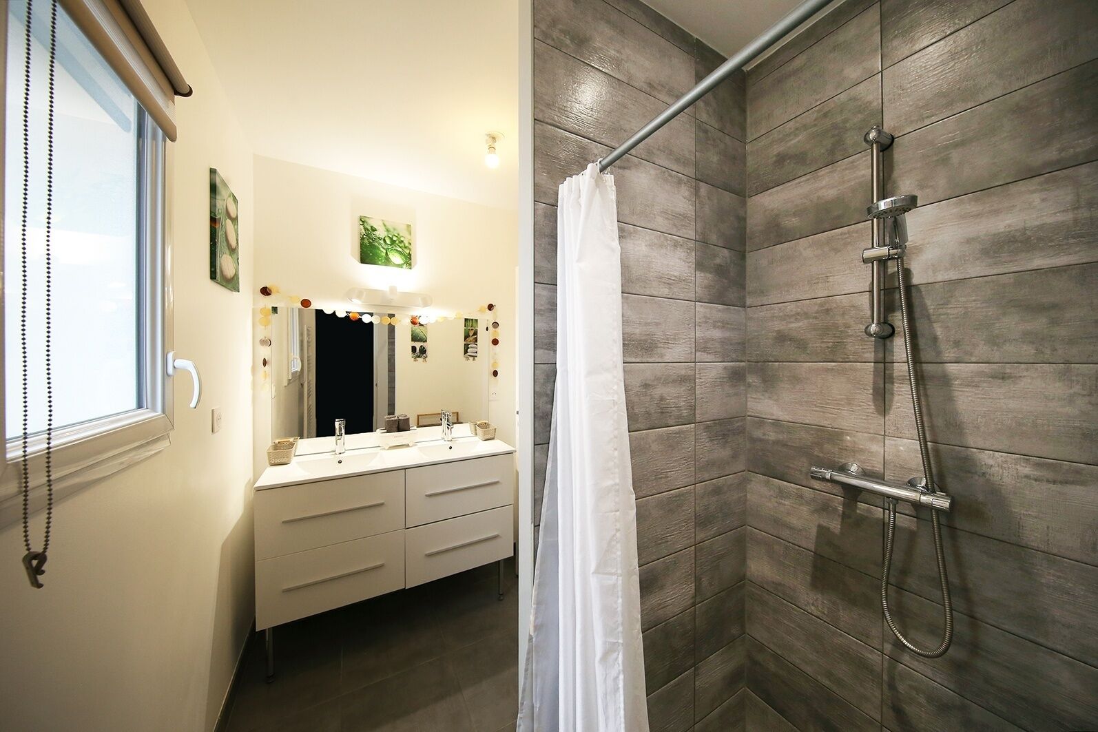 A bathroom with a shower, a vanity with a mirror, and a window with blinds.