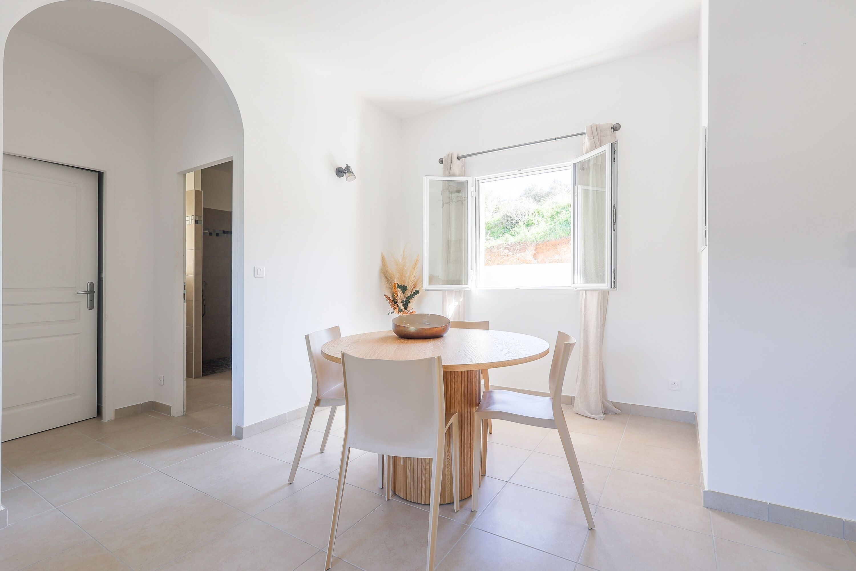 A dining area with a round table, white chairs, and a bowl on the table.