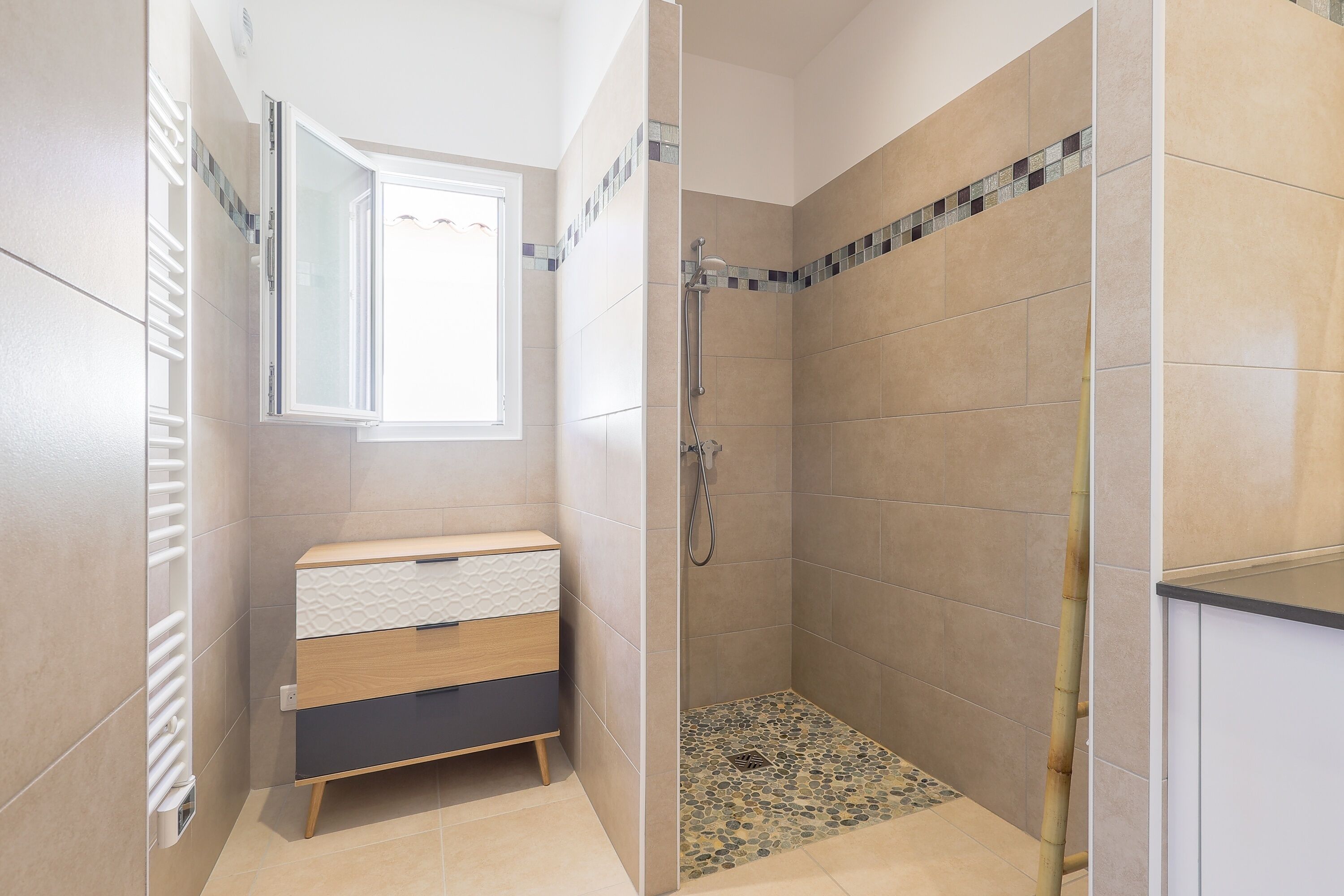 Un baño moderno con ducha, tocador con cajones y ventana que proporciona luz natural.