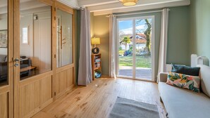 A room with a wooden wardrobe, a sofa with a patterned pillow, a lamp, and a view of the outdoors through a glass door. - La Senpere - Avec sauna entre Océan & Montagnes (Saint-Pée-sur-Nivelle)