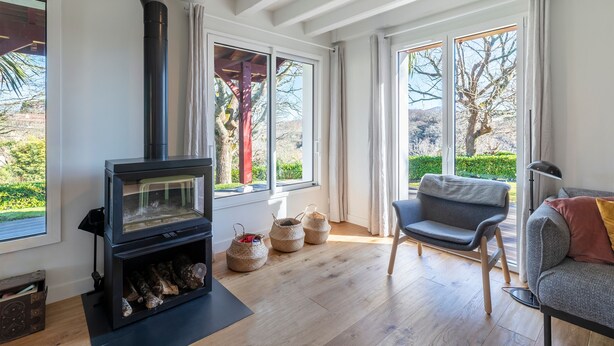A modern living room with a wood-burning stove, large windows, a sofa, and a view of the outdoors. - La Senpere - Avec sauna entre Océan & Montagnes (Saint-Pée-sur-Nivelle)