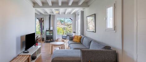 Una sala de estar moderna con un sofá seccional, un televisor de pantalla plana, una chimenea y ventanas amplias con vistas al exterior.