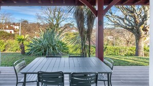 A covered outdoor area with a wooden table and chairs, surrounded by greenery and trees. - La Senpere - Avec sauna entre Océan & Montagnes (Saint-Pée-sur-Nivelle)