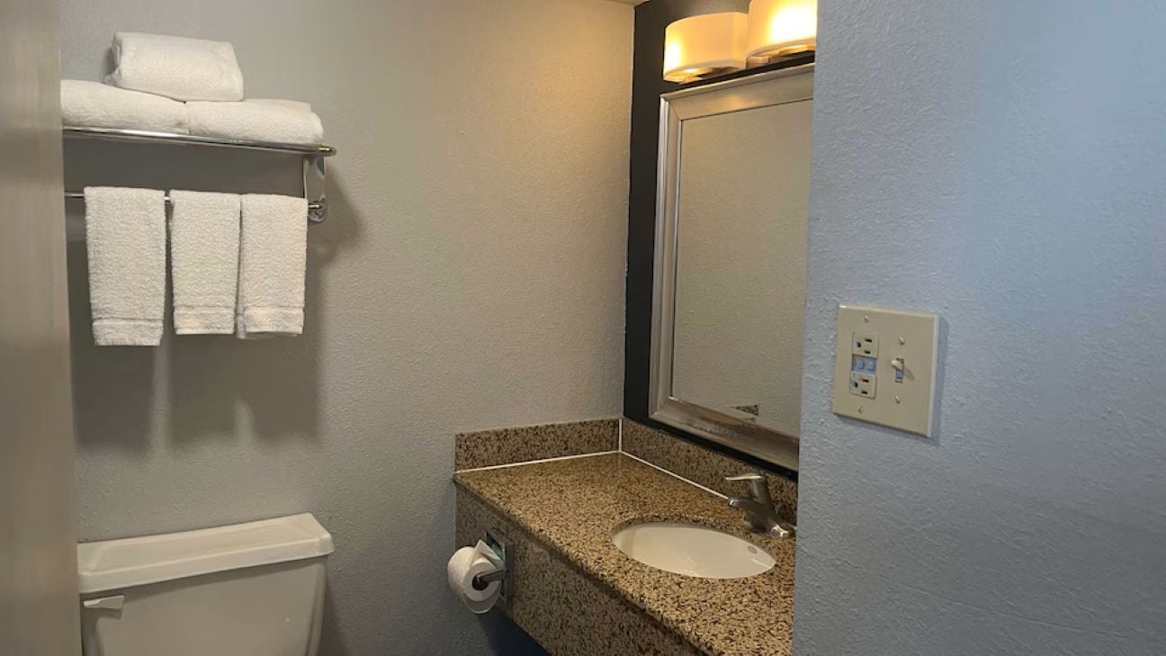 A bathroom with a toilet, sink, towel rack, and a mirror.
