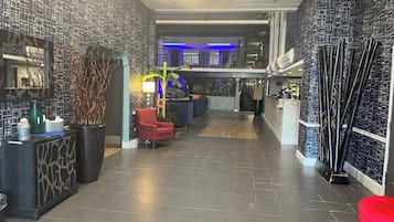 A hotel lobby with a modern design, featuring a reception desk, seating area, and a staircase leading to an upper level.