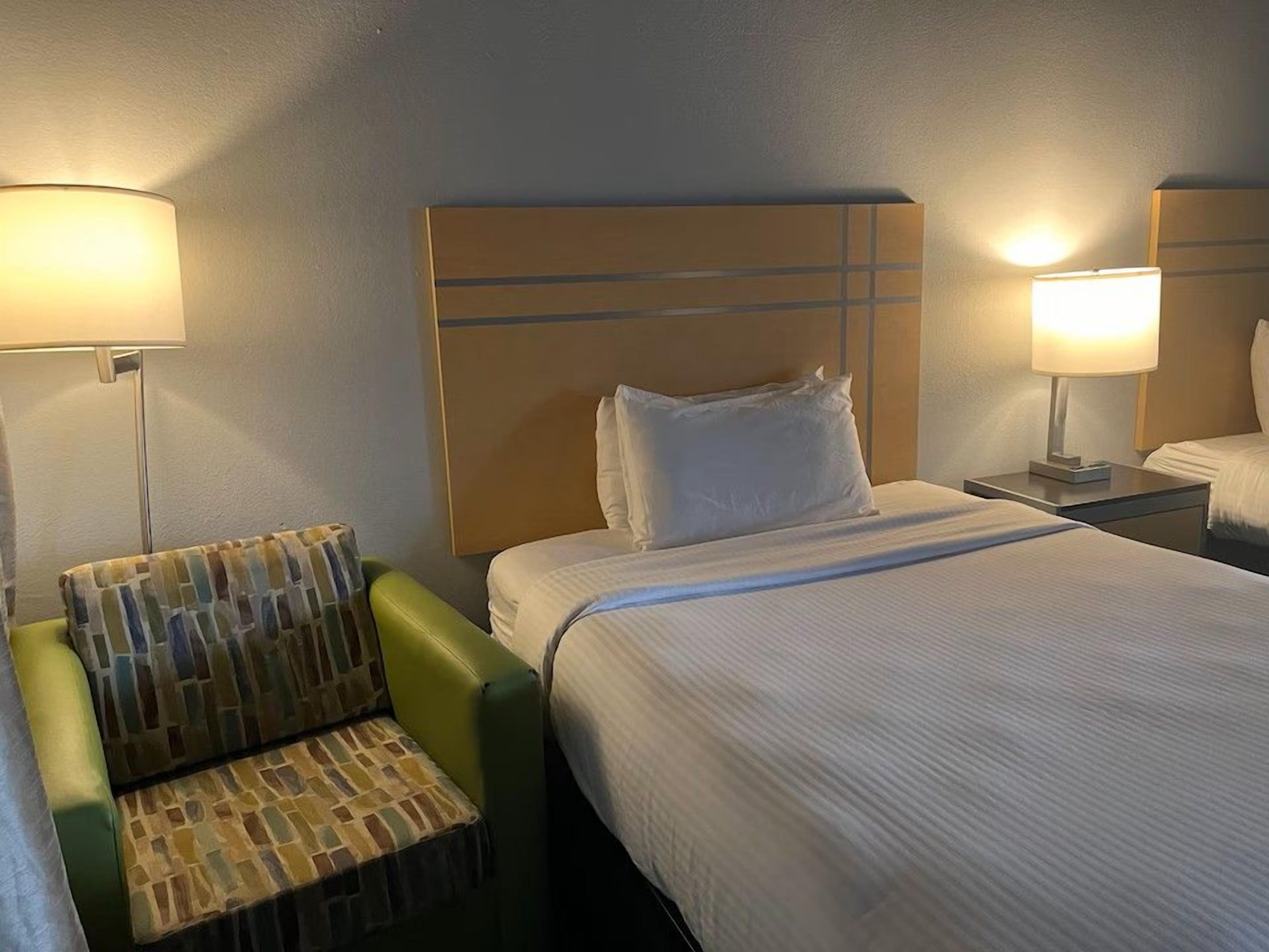Una habitación de hotel con una cama, un sillón verde y dos lámparas de noche.