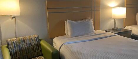 Una habitación de hotel con una cama, un sillón verde y dos lámparas de noche.