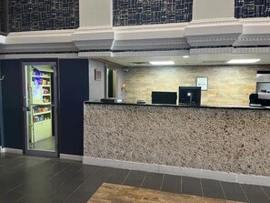 Un espace d’accueil avec un mur en pierre, un comptoir de réception et une porte donnant sur une pièce à l’intérieur verdoyant.