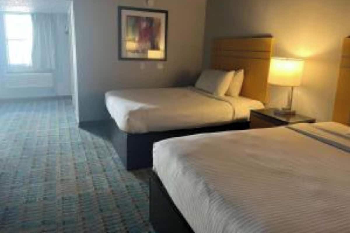 A hotel room with two beds, a nightstand, a lamp, and a painting on the wall.