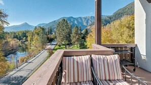 A balcony with a view of a river and mountains, a wooden bench, and a metal cart. - Best Views in Leavenworth from Downtown 2-bedroom Condo (Leavenworth)